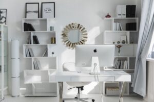 Bright minimalist home office setup with white shelves, desk, and iMac. Ideal for productivity.